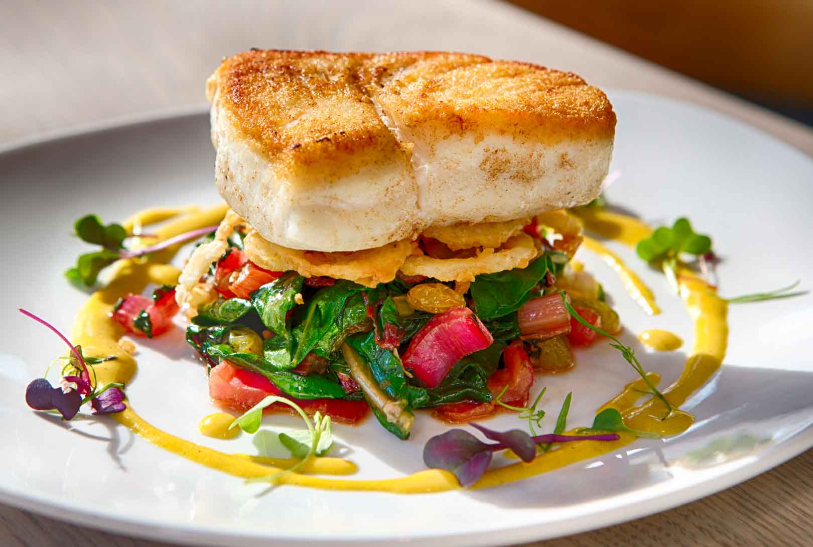 Fish plated with Swiss chard, bacon, pickled golden raisin, and charred tomato