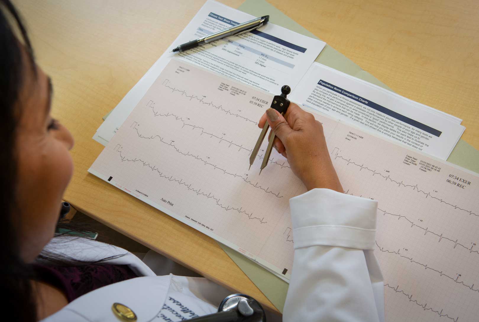 A female doctor reviews an EKG medical chart from patient's physical with a tool at her office desk
