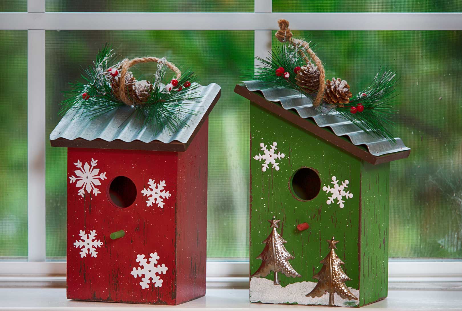 two holiday snowflake-painted birdhouses one in red and one in green with tin roofs