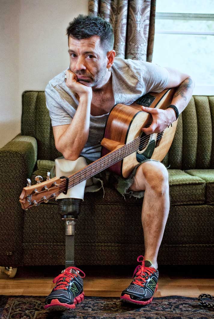 cancer amputee Travis Meadows with his guitar sitting on a green retro couch