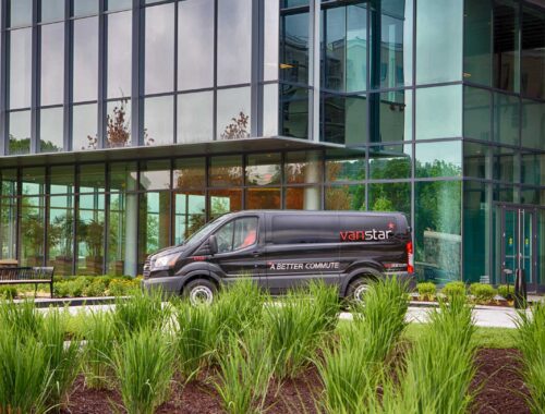A black commuter van photographed in front of a tall glass building