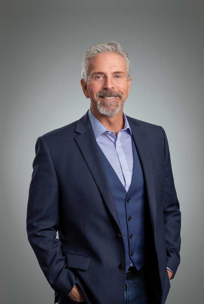 corporate headshot of executive Alex Arnet in a blue suit and vest photographed on a gray backdrop