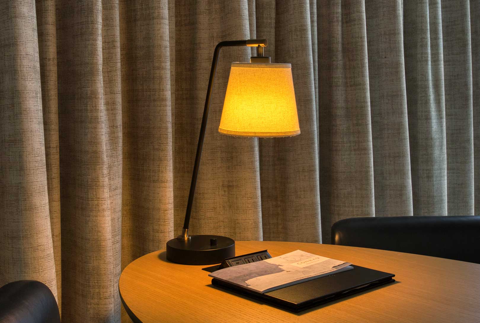 a small desk lamp on a desktop in a room with beige curtains