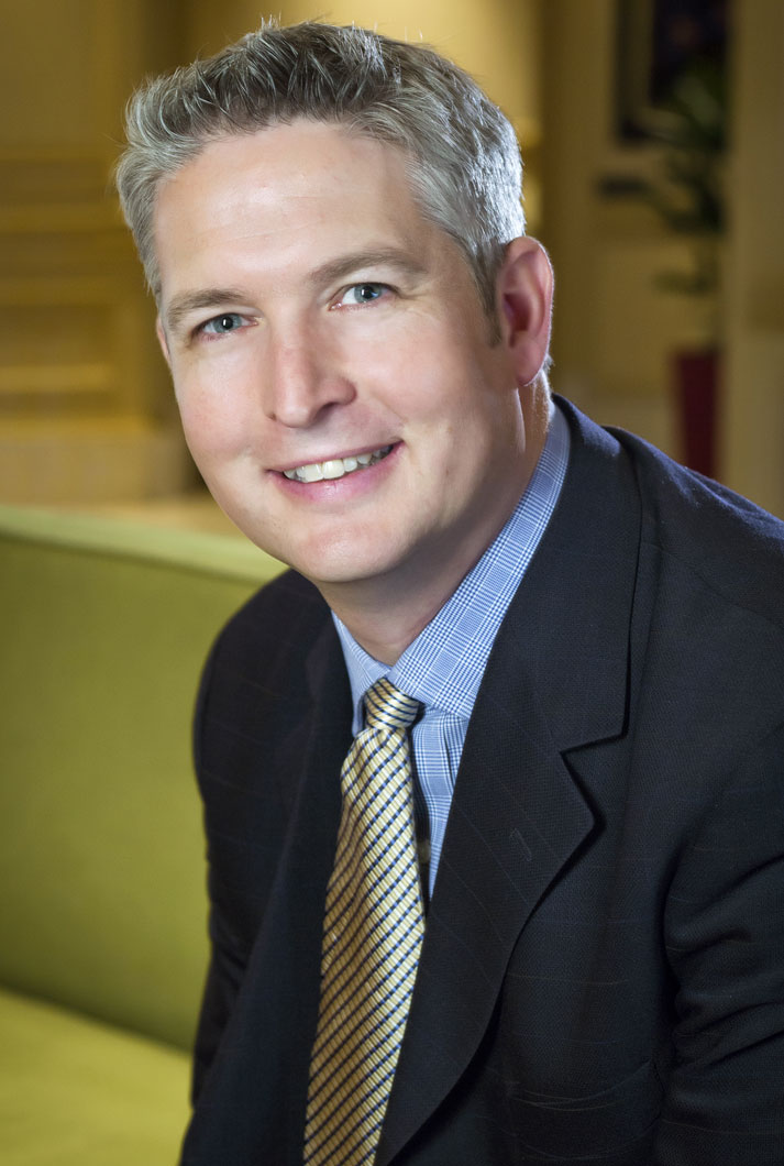 executive headshot of a male executive in suit with gold tie in room with c=green couch