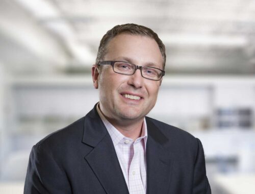 corporate headshot of John Kentzer ina a suit jacket wearing glasses