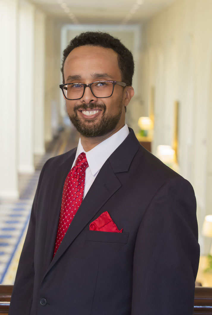 environmental headshot of man in dark suit with red tie and handkerchief