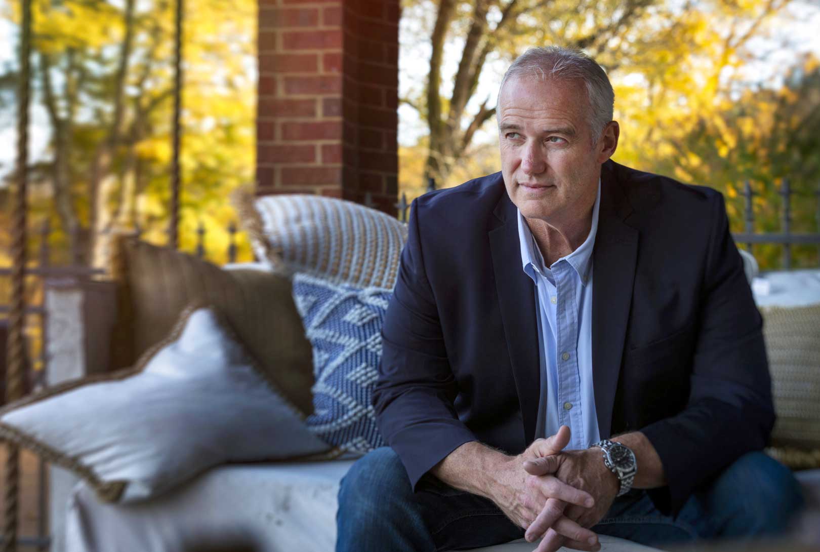 An environmental portrait of Executive Lerry Wilson in a suit jacket and blue shits at his home sitting on his patio