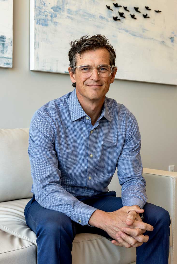 executive headshot of Matthew Miller sitting on a white couch in the waiting room of clinic