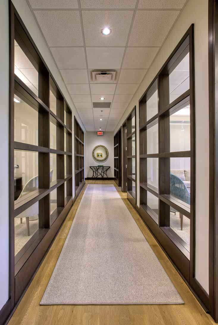 office space corridor with carpet leading to table and mirror with wood-trimmed glass
