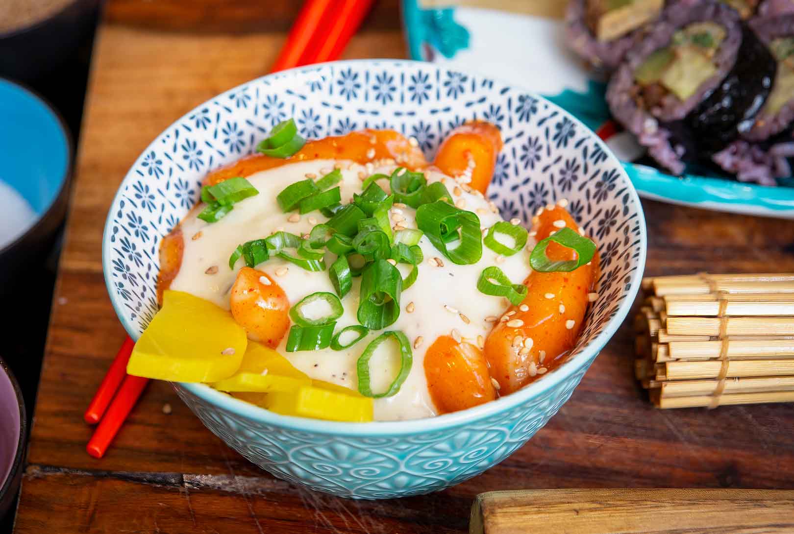 tteokbokki with sticky rice flour topped with sauce cheese green onions and a yellow pickled radish