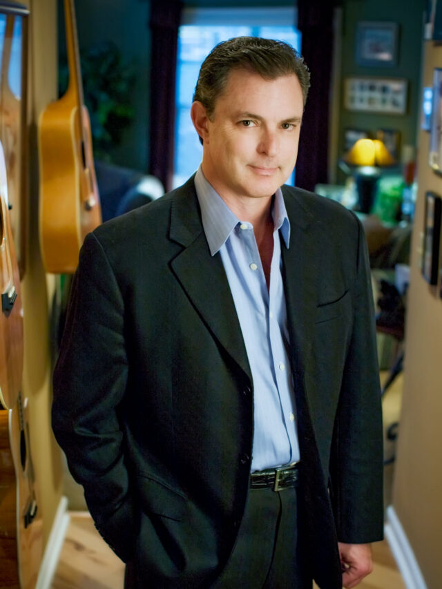 A man in a suit standing in front of guitars.