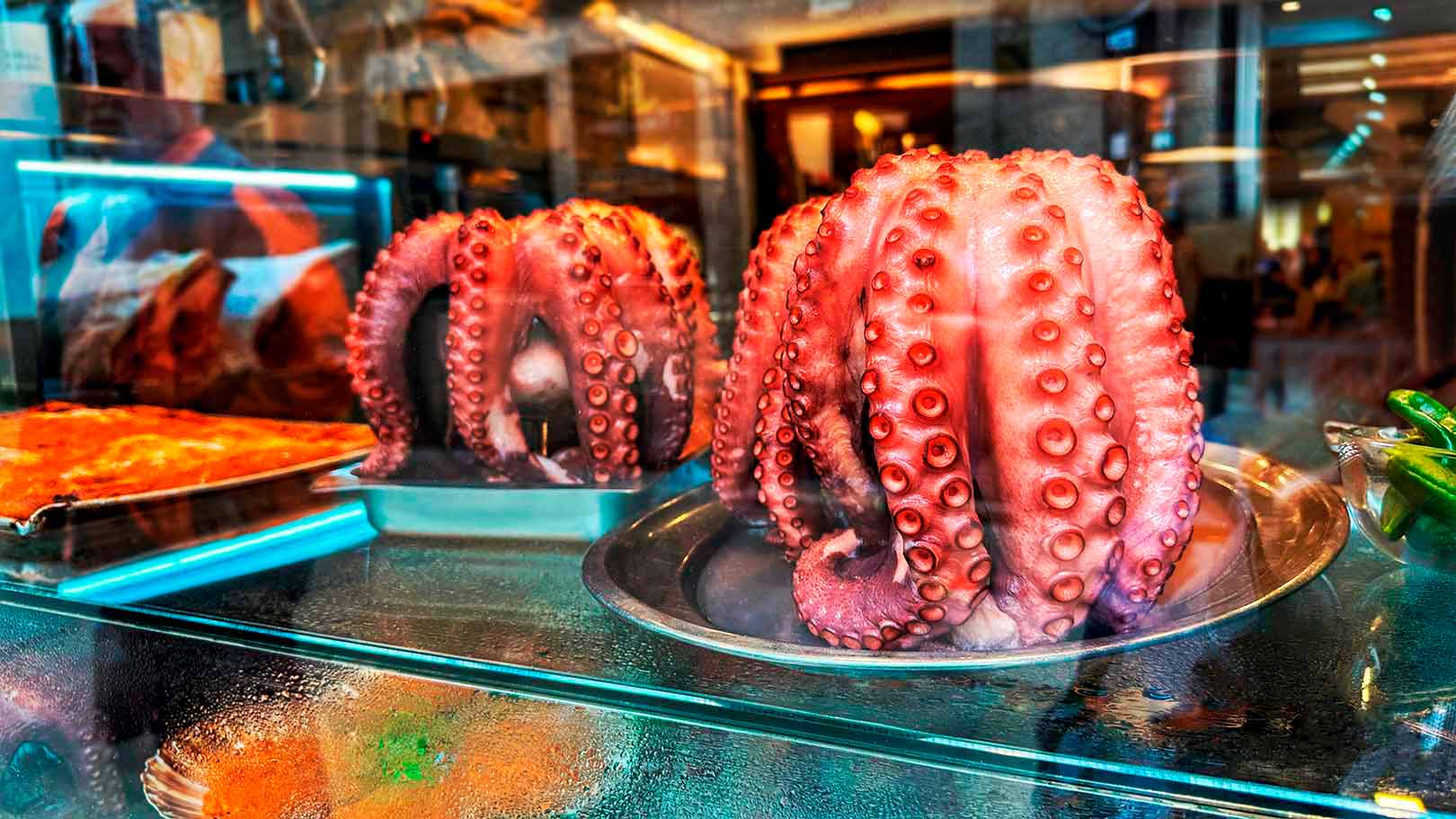 Two large octopus tentacles displayed on metal trays behind a glass case in a food establishment.