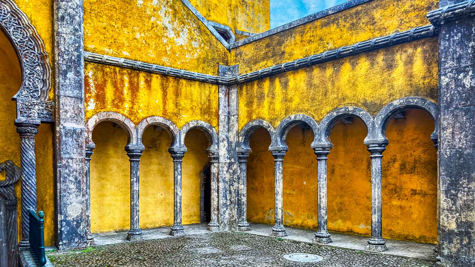 An outdoor corridor with curved arches of stone columns and yellow aged walls at the Sintra Palace in Portugal.